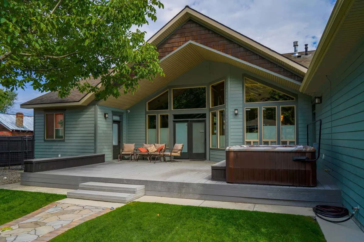 A welcoming deck area with a 6-person hot tub and comfortable seating, framed by large windows and outdoor scenery. The setting invites relaxation after an active day, whether skiing or golfing.