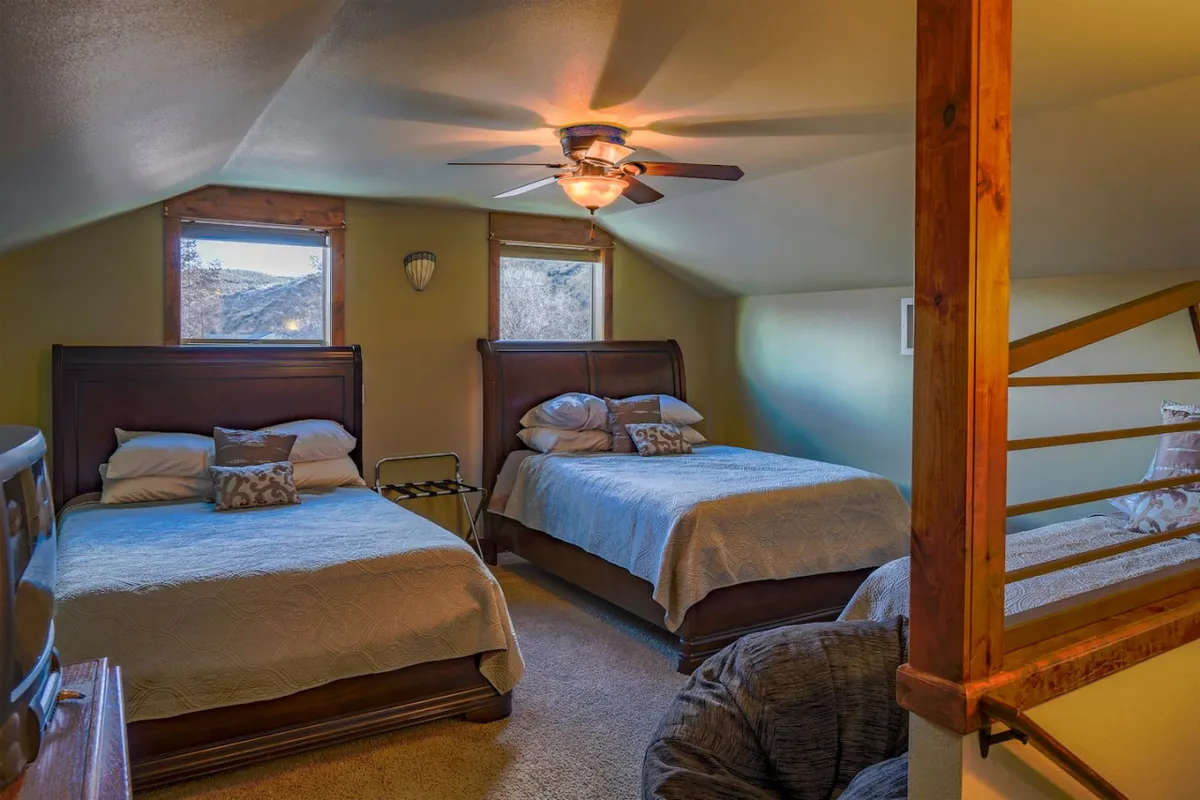 A welcoming bedroom featuring two queen beds, ceiling fan, and large windows offering scenic views. The room exudes warmth and is designed for flexible sleeping arrangements, suitable for families or groups.