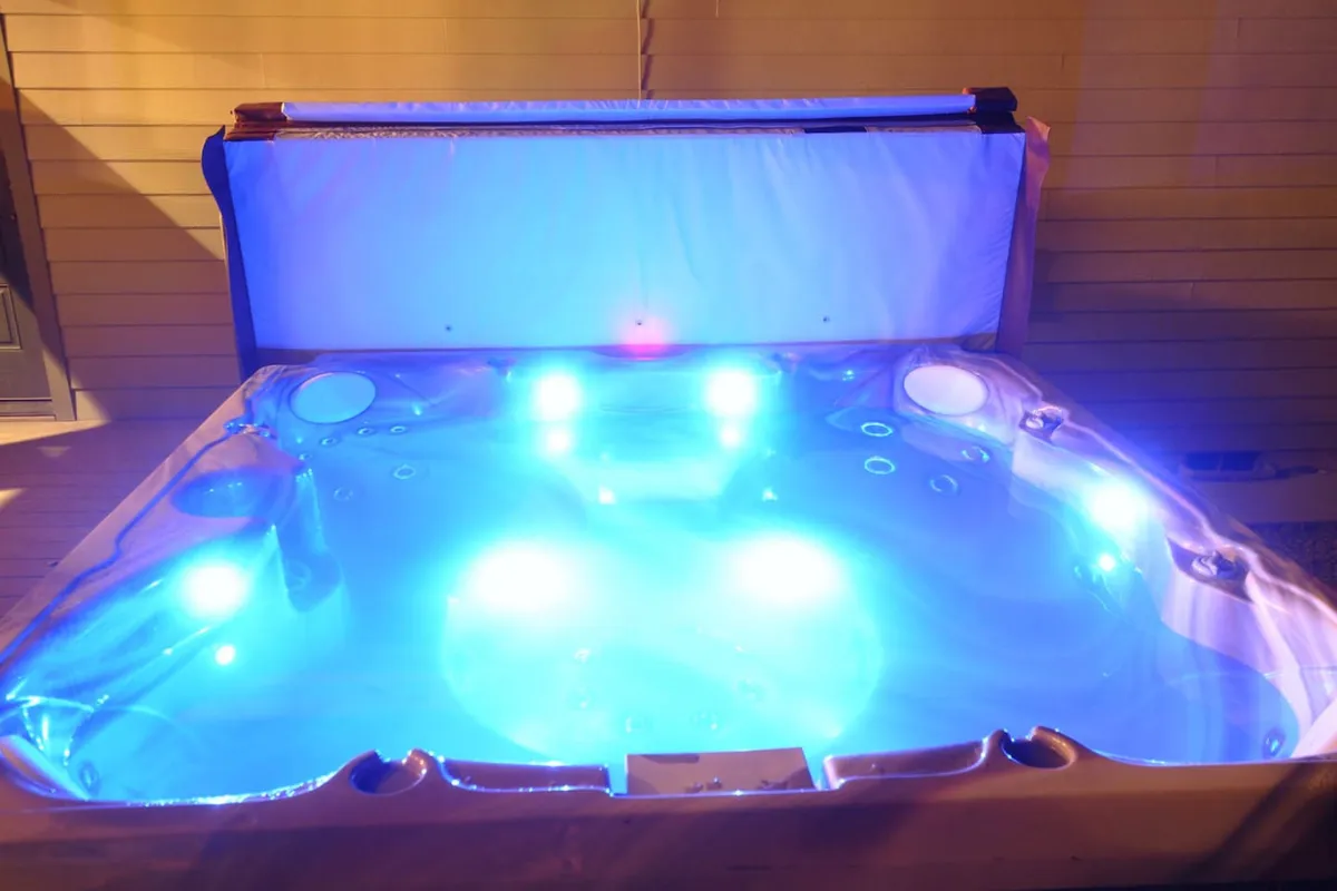 A modern indoor hot tub illuminated with LED lights, its calm water surface hinting at the serene experience it provides. The setting is intimate and inviting, ideal for relaxation and socializing after a long day.