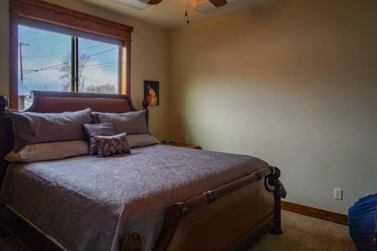 A tranquil bedroom with a neatly made bed, decorative pillows, a window allowing natural light to fill the space, and subtle artwork on the wall. The room feels calm and inviting, highlighting comfort and restful ambiance.