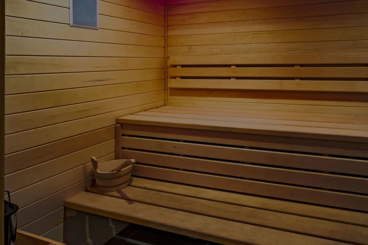 A view inside a traditional sauna room featuring wooden benches, a sauna bucket, and warm wooden walls. The atmosphere feels calming and restorative, suggesting soothing heat and a peaceful break from daily routines.