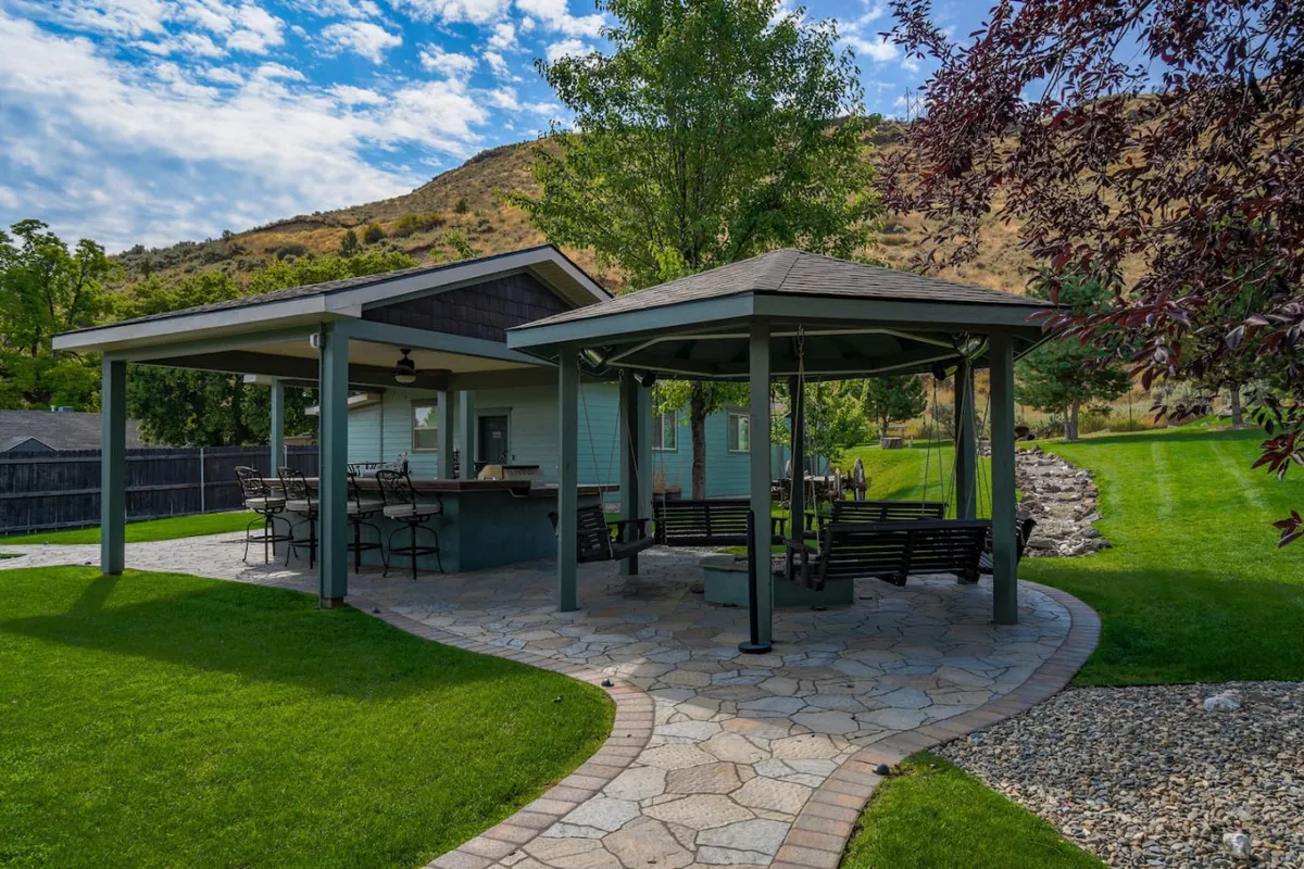 A beautifully landscaped exterior featuring a pavilion with ample seating, an outdoor bar area, and mountain vistas. The space is designed for relaxation, social gatherings, and enjoying the natural beauty of the surroundings.