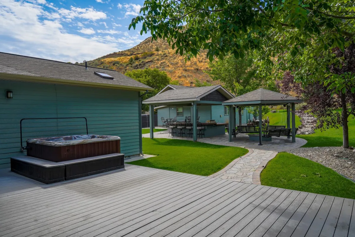 A beautifully landscaped backyard with a hot tub, stone pathway, gazebo, and lush green lawn. The setting is ideal for outdoor relaxation, social gatherings, and enjoying nature right at home.